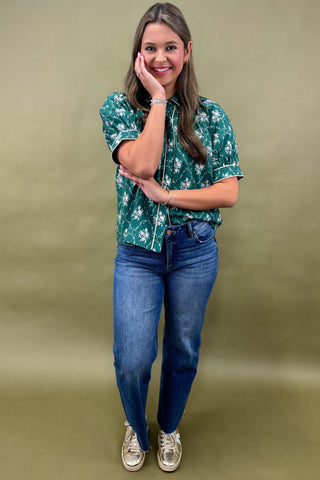 Woman wearing a green floral blouse and blue jeans against a beige background