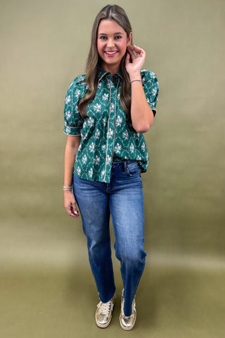 Woman wearing a green floral blouse and blue jeans against a beige background