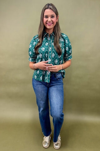 Woman wearing a green floral shirt and blue jeans against a beige background