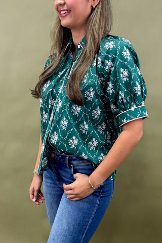 Woman wearing a green patterned blouse and blue jeans against a green background