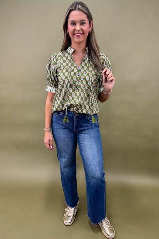Woman wearing a patterned blouse and blue jeans against a beige background