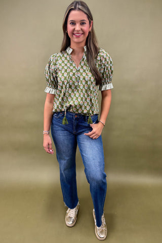 Woman wearing a green patterned blouse and blue jeans against a beige background