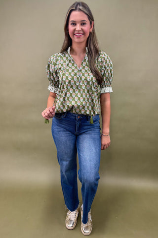 Woman wearing a green floral blouse and blue jeans against a beige background