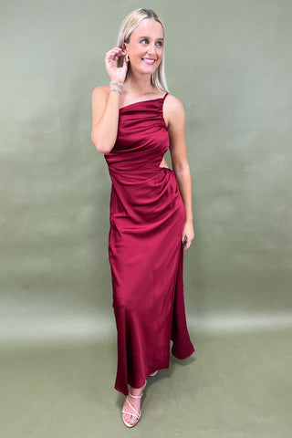 Woman wearing a burgundy evening gown against a plain background