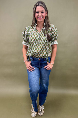 Woman wearing a green floral blouse and blue jeans against a beige background