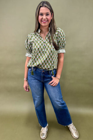 Woman wearing a green floral blouse and blue jeans against a beige background