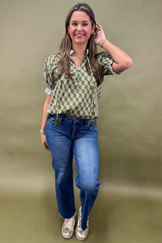 Woman wearing a patterned blouse and blue jeans against a green background
