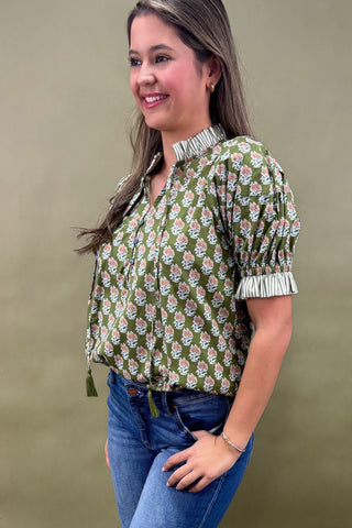 Woman wearing a green floral blouse and blue jeans against a beige background
