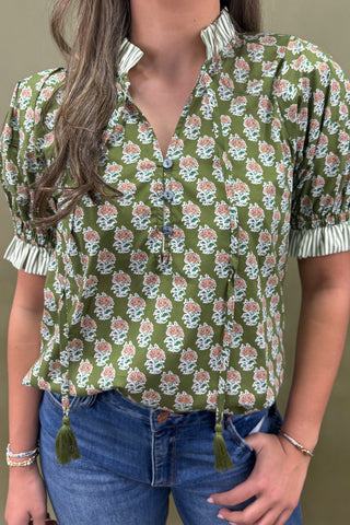 Woman wearing a green floral blouse with tassel details against a neutral background