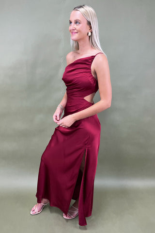 Woman wearing a burgundy evening gown with a cut-out design on a plain background