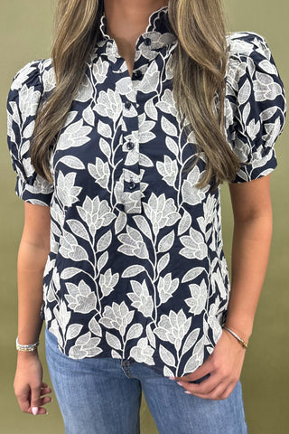 Woman wearing a navy blue floral patterned blouse against a green background