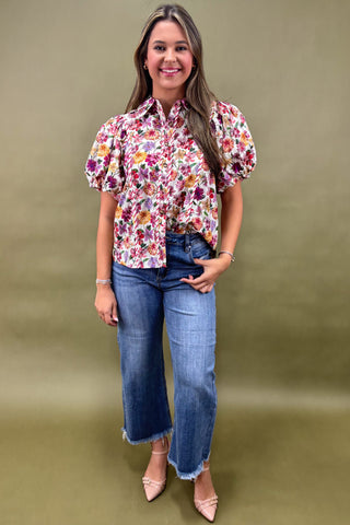 Woman wearing a floral blouse and jeans against a green background