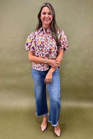Woman wearing a floral blouse and jeans against a green background