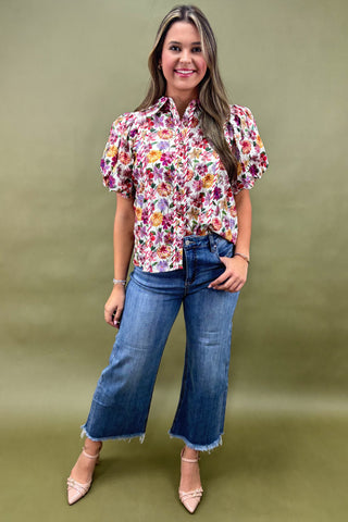 Woman wearing a floral blouse and blue jeans against a green background
