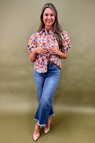 Woman wearing a floral blouse and jeans against a plain background