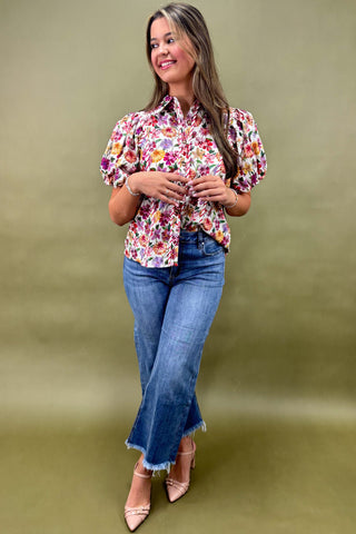 Woman wearing a floral blouse and blue jeans against a green background