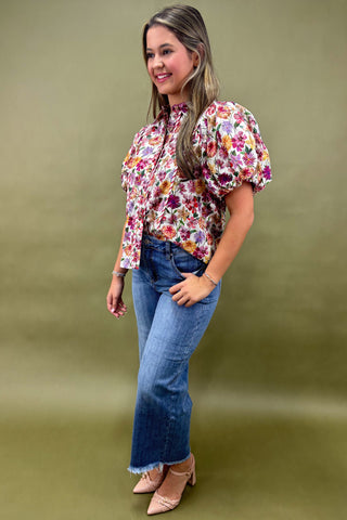Woman wearing a floral blouse and blue jeans against a green background