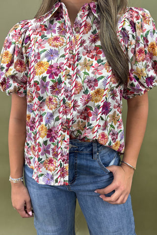 Person wearing a colorful floral blouse and blue jeans against a green background