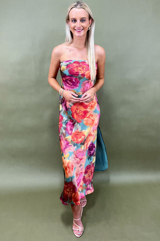 Woman wearing a colorful floral strapless dress against a plain background