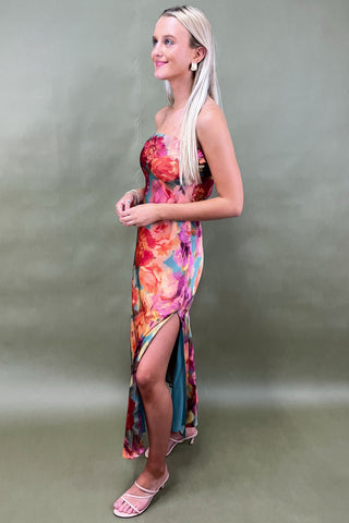 Woman wearing a colorful floral dress with a slit on a plain background