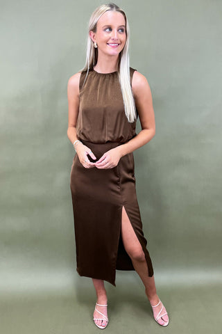 Woman wearing a brown sleeveless dress with a slit on a green background