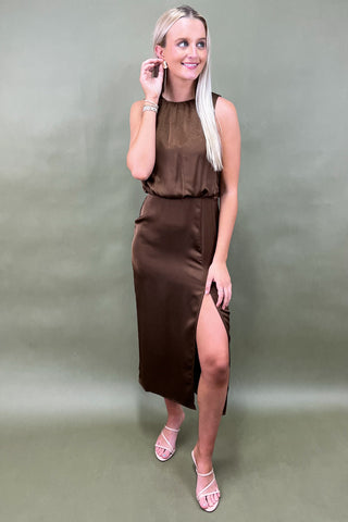 Woman wearing a brown dress with a slit on a plain background
