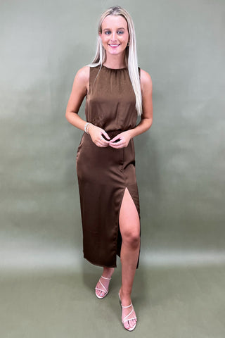 Woman wearing a brown dress with a slit on a plain background