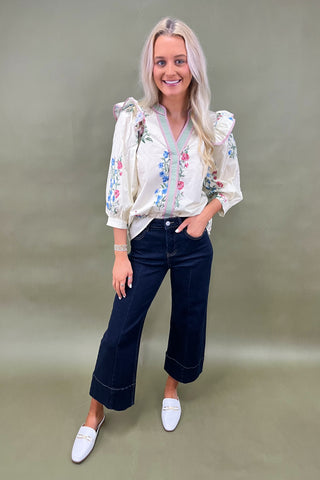 Woman wearing a floral blouse and dark jeans against a plain background
