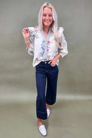 Woman wearing a floral blouse and dark jeans on a plain background