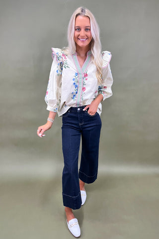 Woman wearing a floral blouse and jeans on a plain background