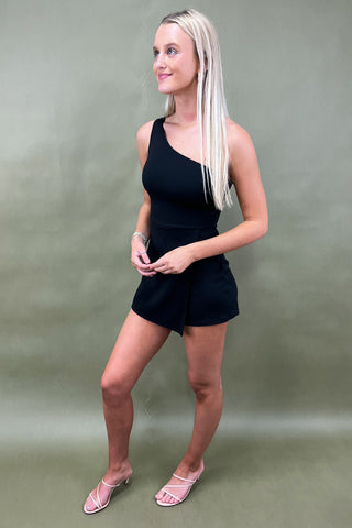 Woman wearing a black romper against a plain background