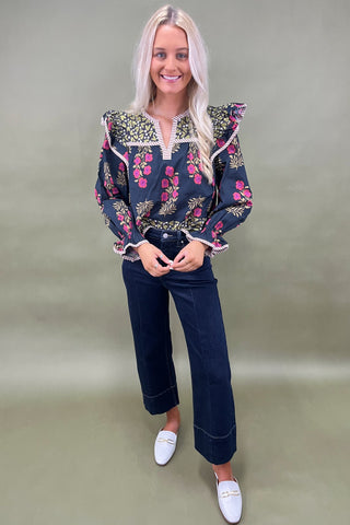 Woman wearing a floral blouse and dark jeans against a plain background