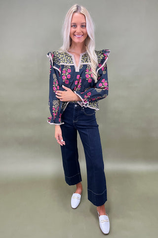 Woman wearing a floral embroidered top and dark jeans on a plain background