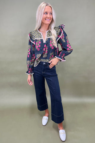 Woman wearing a floral embroidered blouse and dark jeans on a plain background