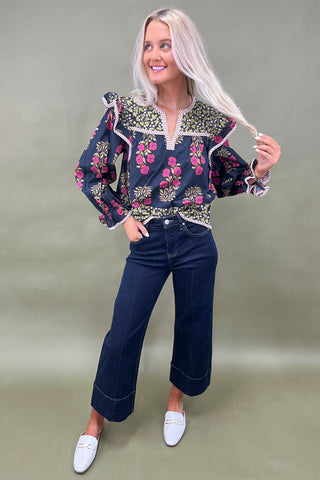 Woman wearing a patterned blouse and jeans against a plain background