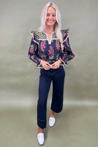 Woman wearing a floral blouse and dark jeans against a plain background