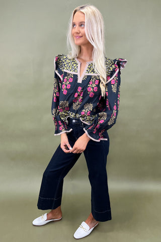 Woman wearing a floral blouse and dark pants against a green background