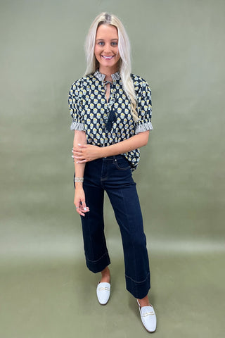Woman wearing a patterned blouse and dark jeans against a green background