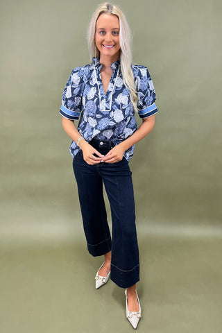 Blue floral blouse with contrast trim and short sleeves paired with dark wide leg cropped jeans and white pointed loafers