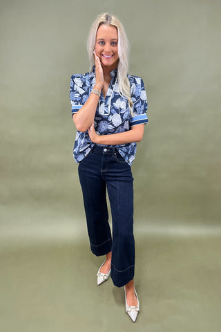 Blue floral blouse with contrast trim and short sleeves paired with dark wide leg cropped jeans and white pointed loafers