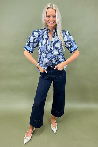 Blue floral blouse with contrast trim and short sleeves paired with dark wide leg cropped jeans and white pointed loafers