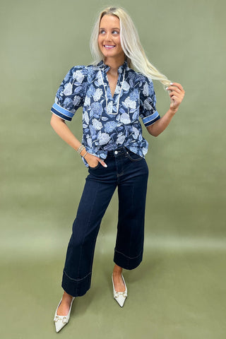Blue floral blouse with contrast trim and short sleeves paired with dark wide leg cropped jeans and white pointed loafers