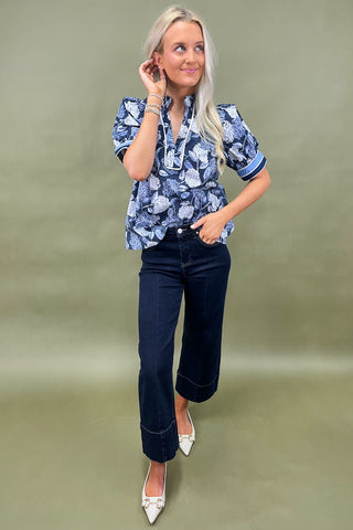 Blue floral blouse with contrast trim and short sleeves paired with dark wide leg cropped jeans and white pointed loafers