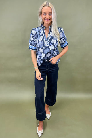 Blue floral blouse with contrast trim and short sleeves paired with dark wide leg cropped jeans and white pointed loafers