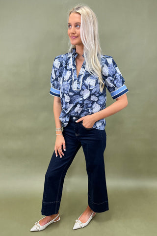 Blue floral blouse with contrast trim and short sleeves paired with dark wide leg cropped jeans and white pointed loafers