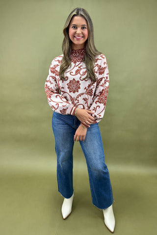Woman wearing a patterned blouse, blue jeans, and white boots on a green background