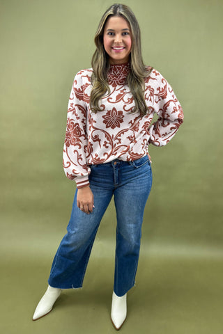 Woman wearing a patterned blouse and jeans on a green background