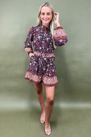 Woman wearing a floral dress with a patterned belt against a green background