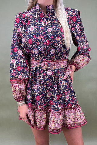 Woman wearing a long-sleeve floral dress with a patterned hem against a neutral background