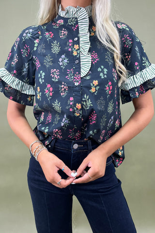 Woman wearing a floral blouse with ruffled details on a plain background